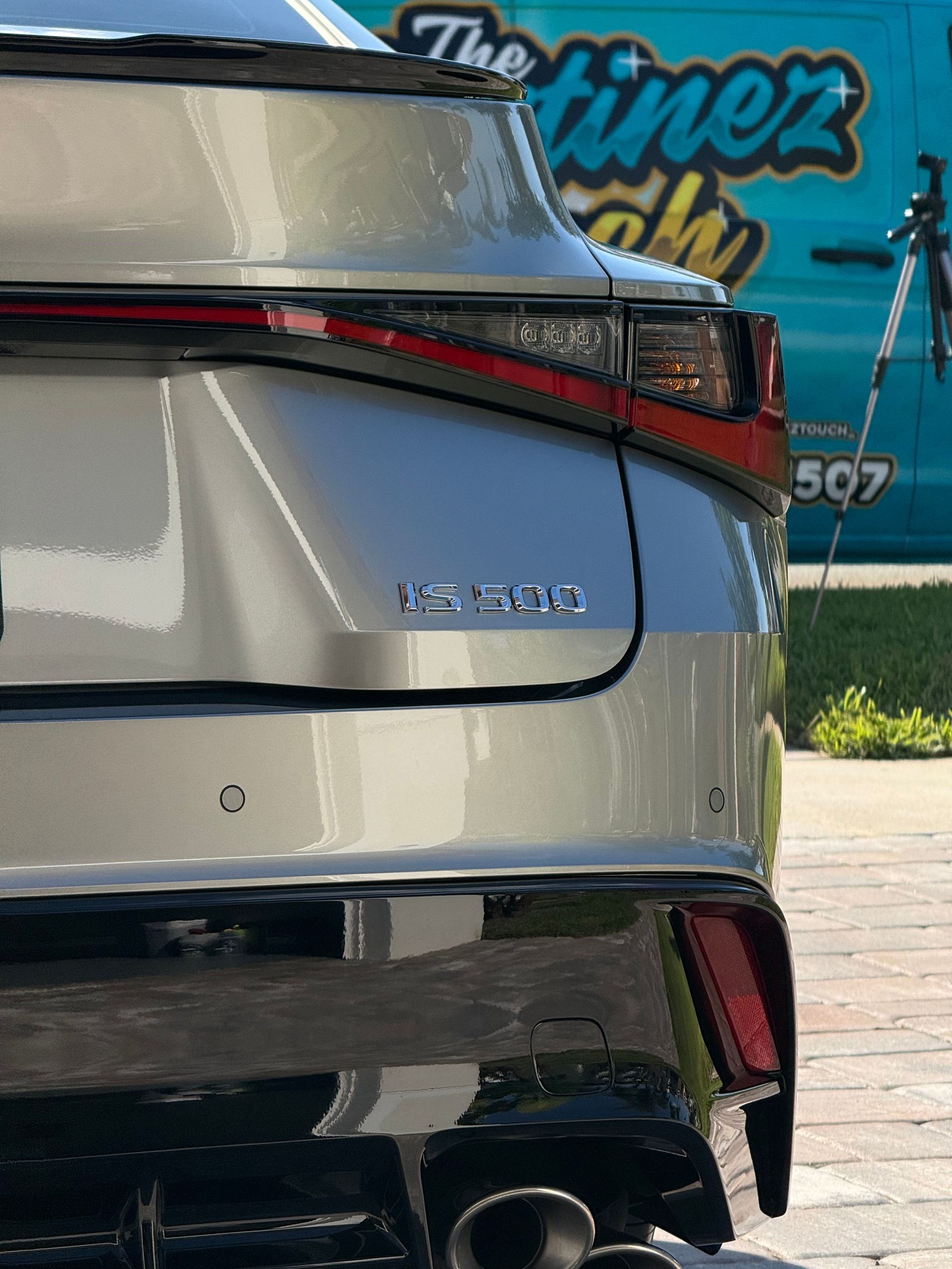 Rear view of a silver Lexus SUV with taillights visible, parked near a blue sign.