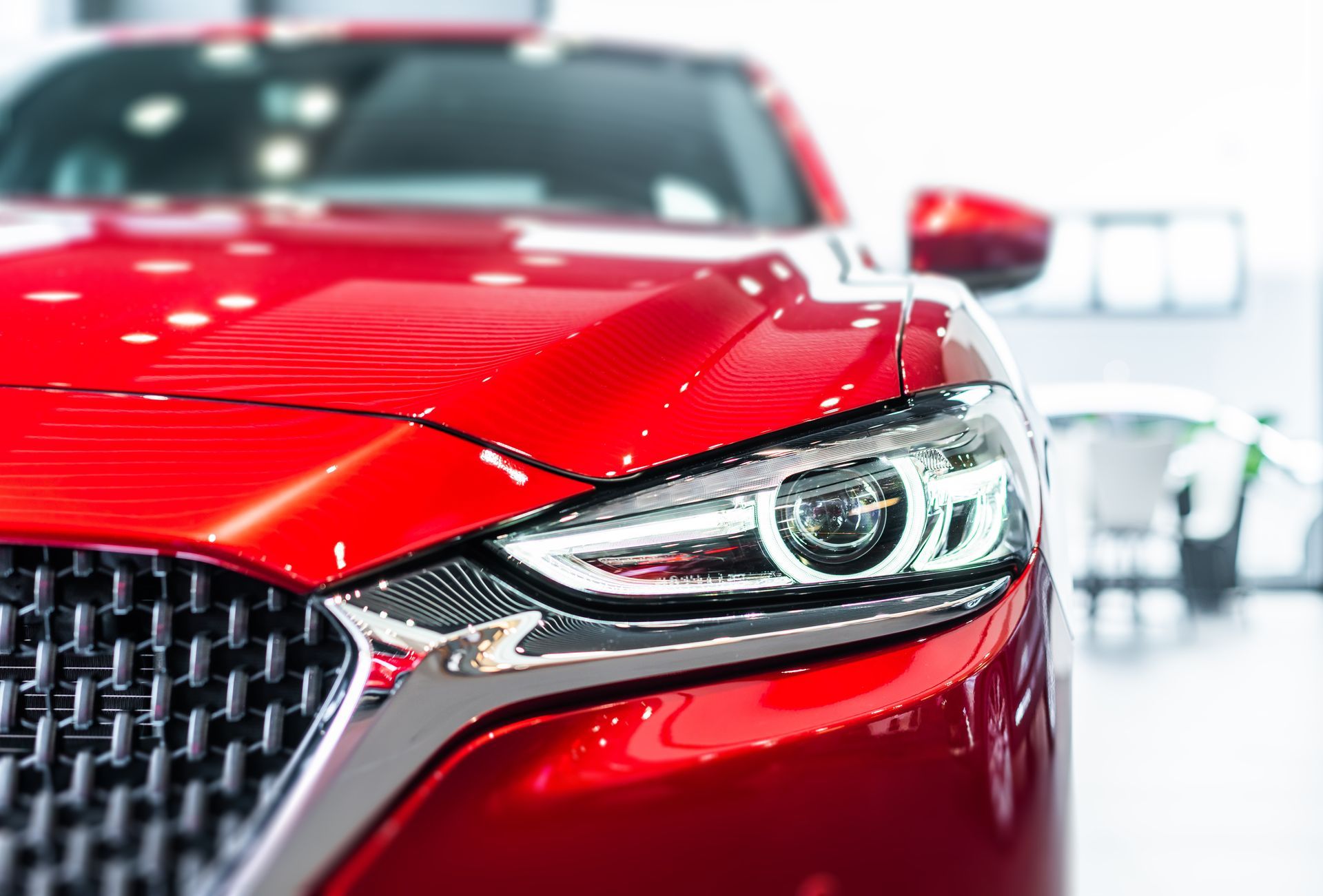 Close-up of a red sports car front headlight and grille in a bright showroom