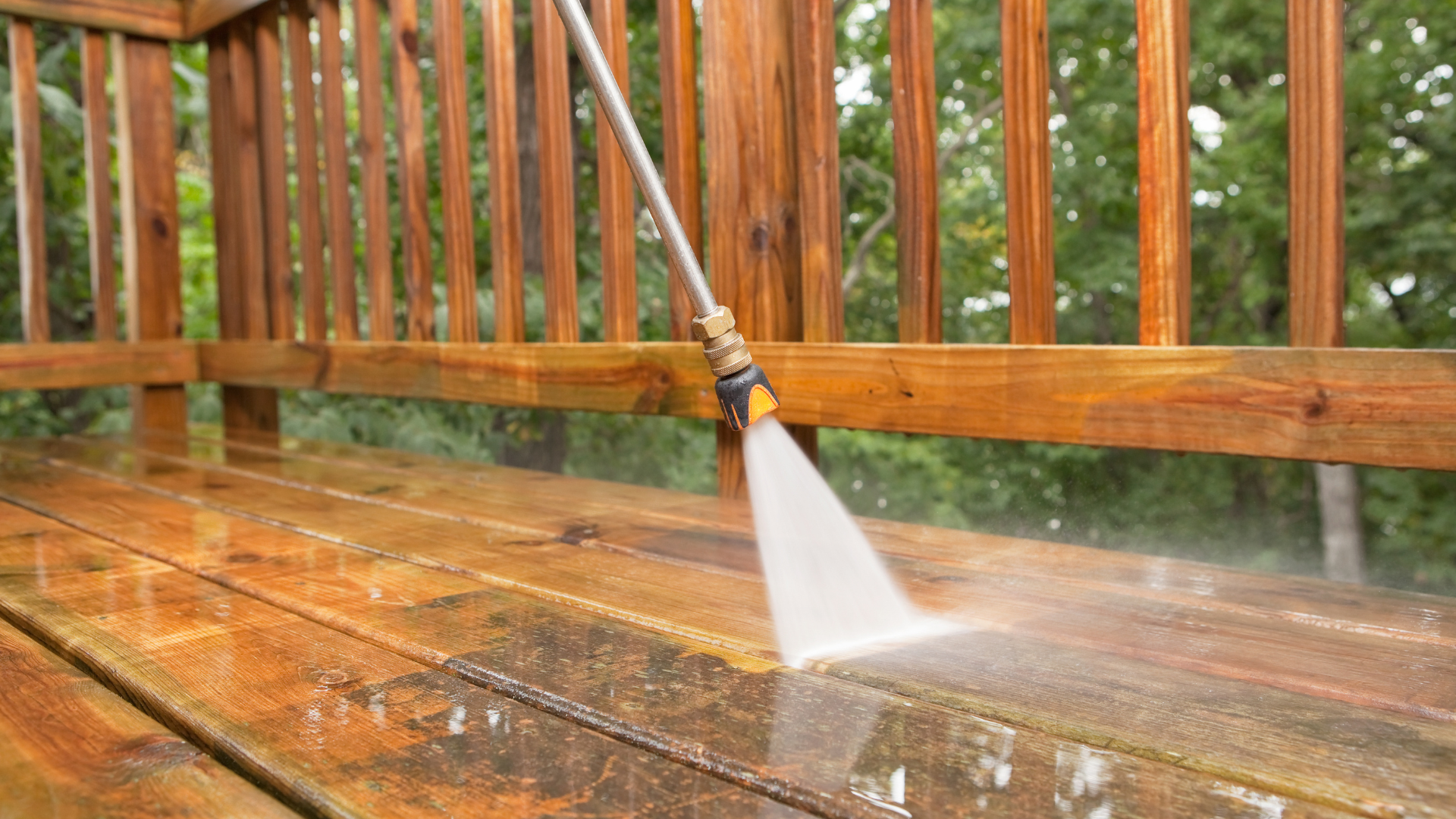 Power washer cleaning a wooden deck, spraying water.