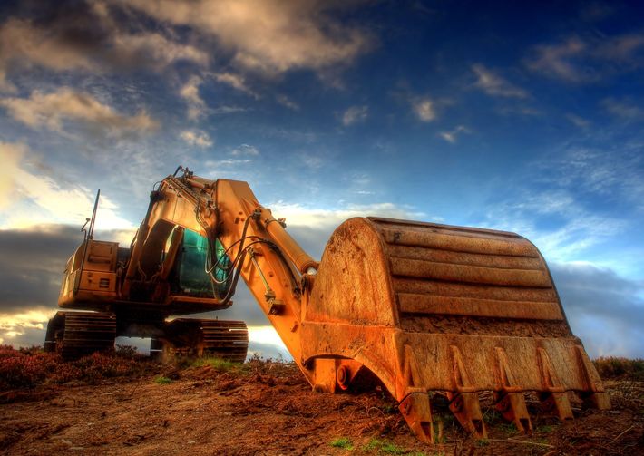 An excavator is sitting in the dirt with a blue sky in the background An excavator is sitting in the dirt with a blue sky in the background