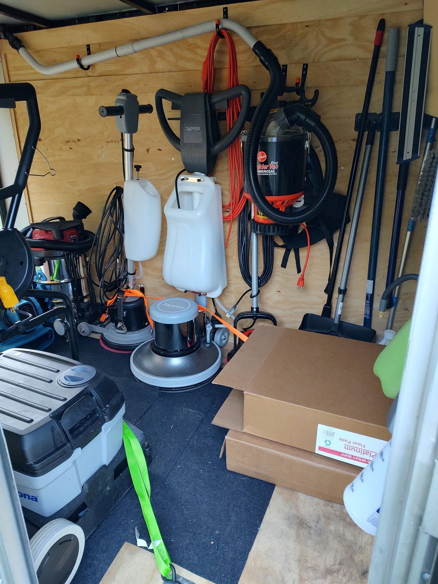 Storage shed with tools, hoses, and lawn equipment, plus stacked boxes and bottles on shelves.