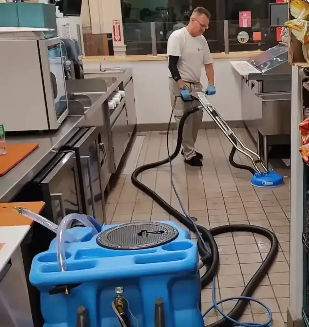Spinning tile cleaning head lifting built-up grime from a commercial kitchen floor along stainless steel equipment