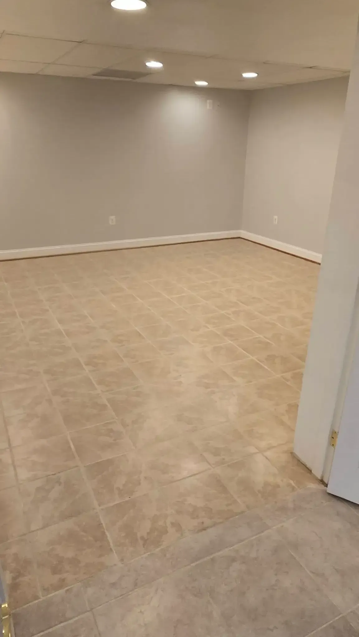 Empty beige tiled room with white walls and recessed ceiling lights, viewed from an open doorway
