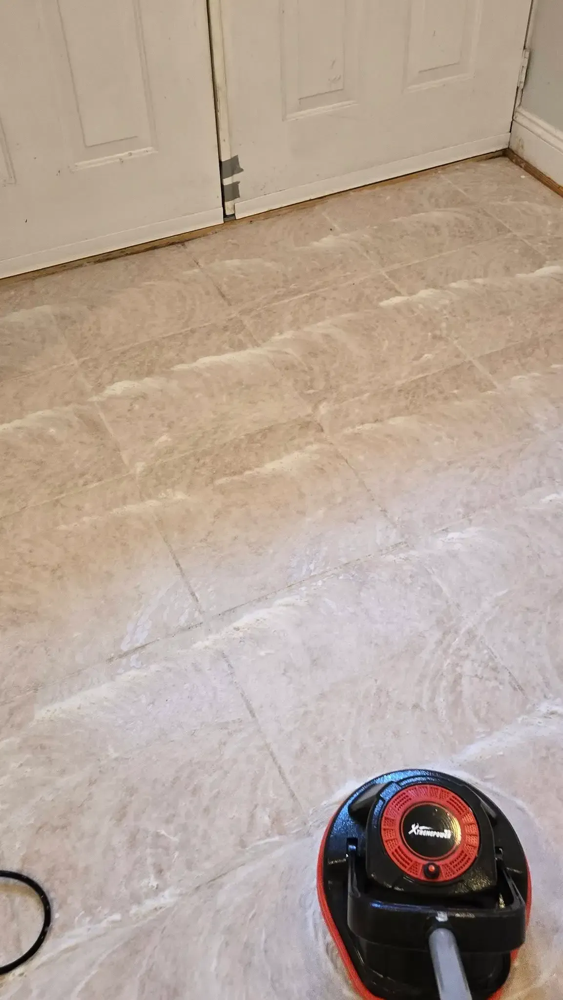 Robot vacuum on a light-colored floor near white double doors.
