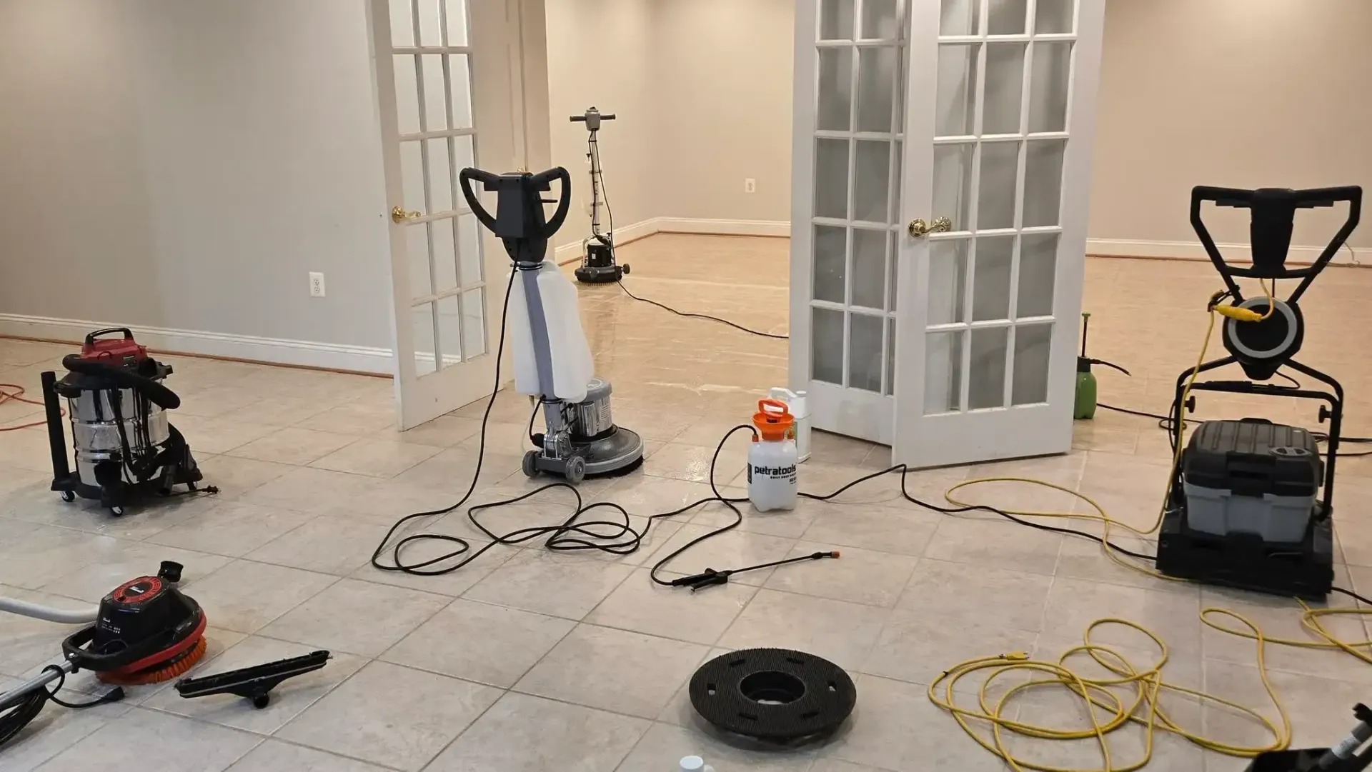 Two exercise machines and cables arranged on a tiled floor in a bright room with French doors.