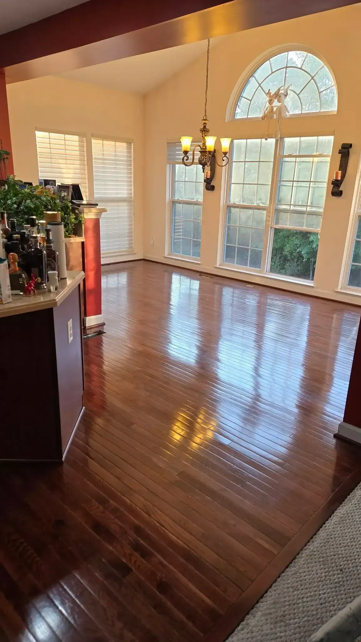 Sunlit living room with hardwood floors, large arched windows, and a fireplace mantel.