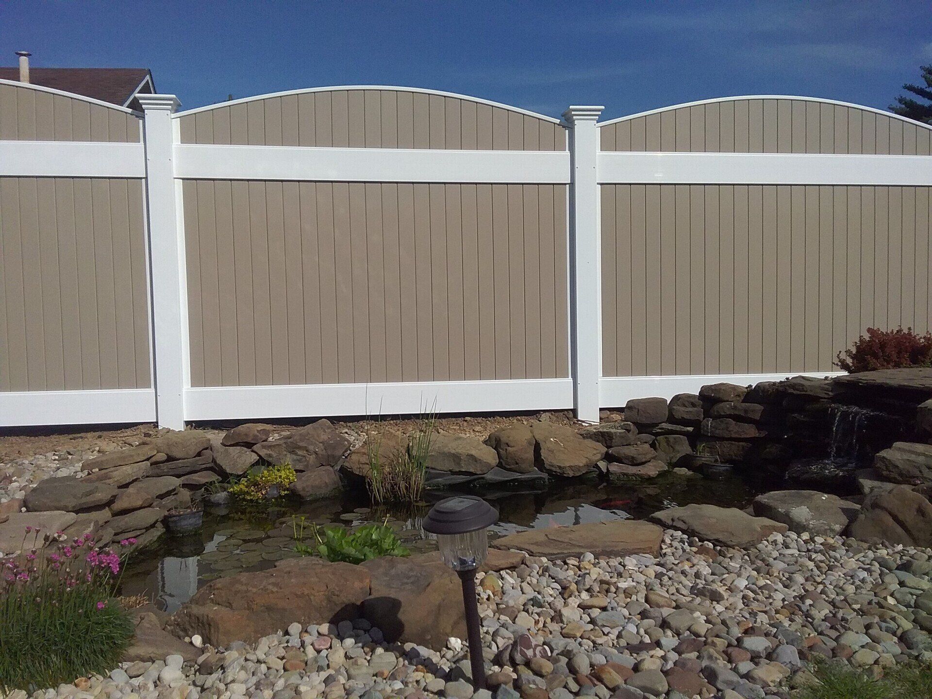 Brown and white fence behind a small pond with rocks and plants.