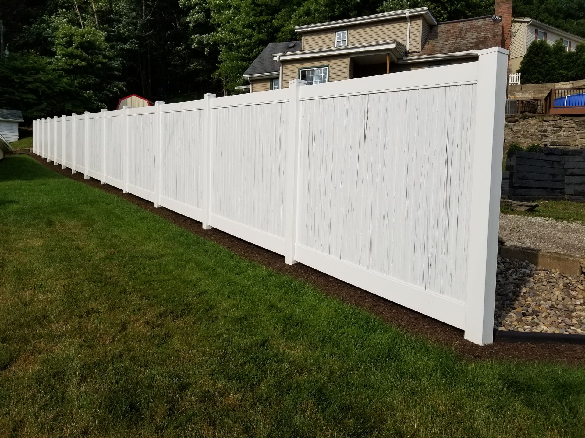 White vinyl privacy fence on green grass, with a house in the background.