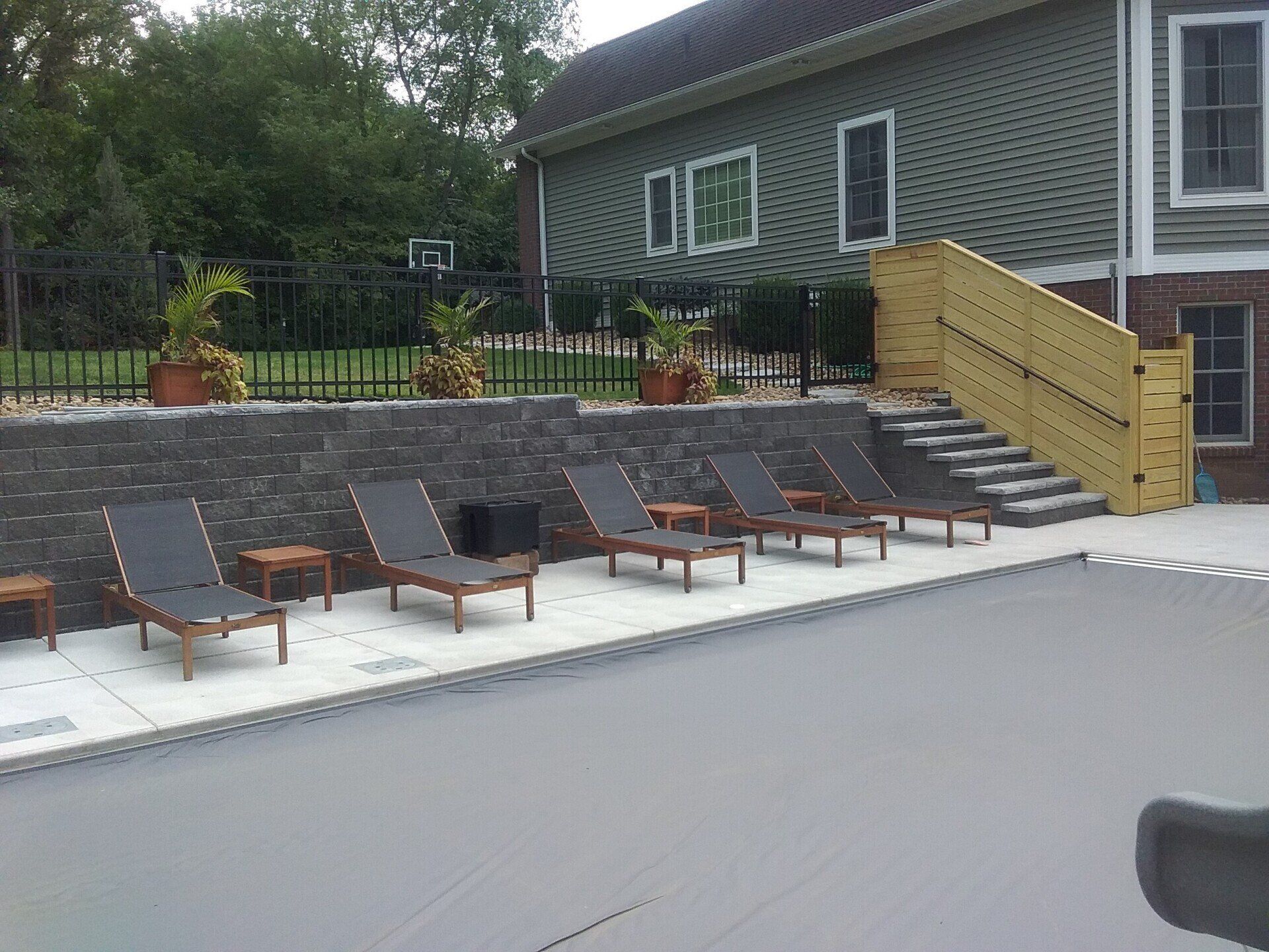 Poolside scene with lounge chairs, retaining wall, stairs, and house.