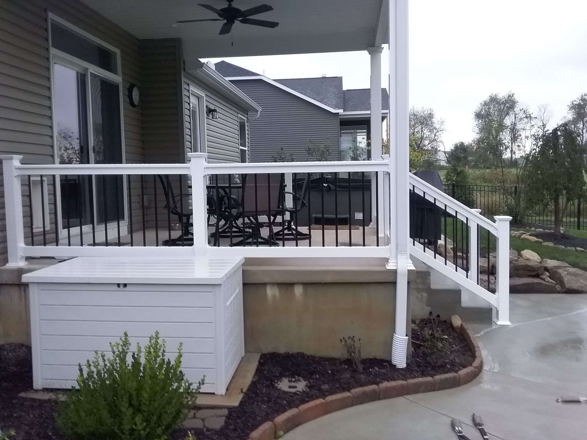 Covered porch with white railings, steps, and storage box. Black accents. Patio furniture visible.