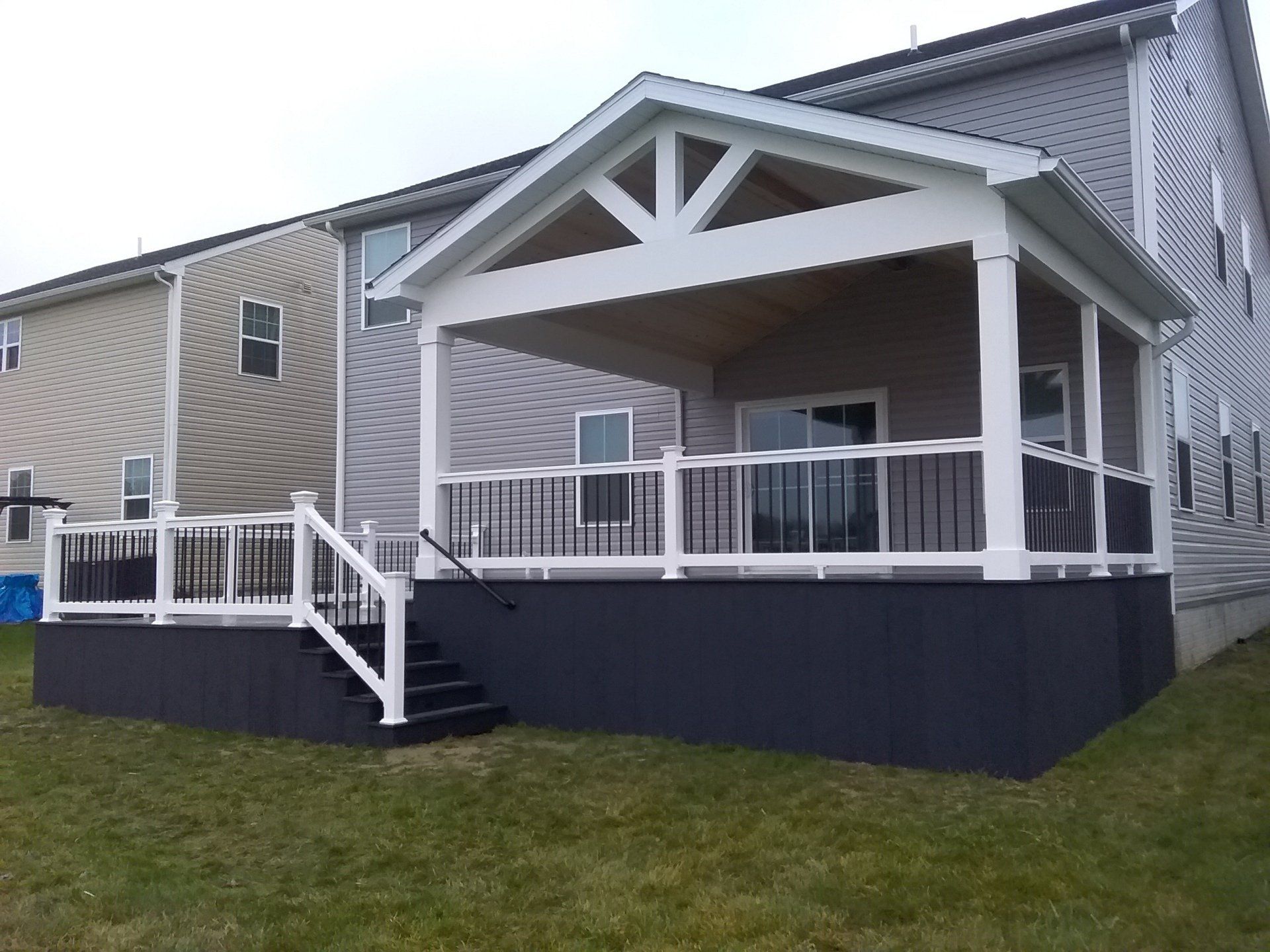 Covered deck with white trim and black accents, attached to a two-story house.