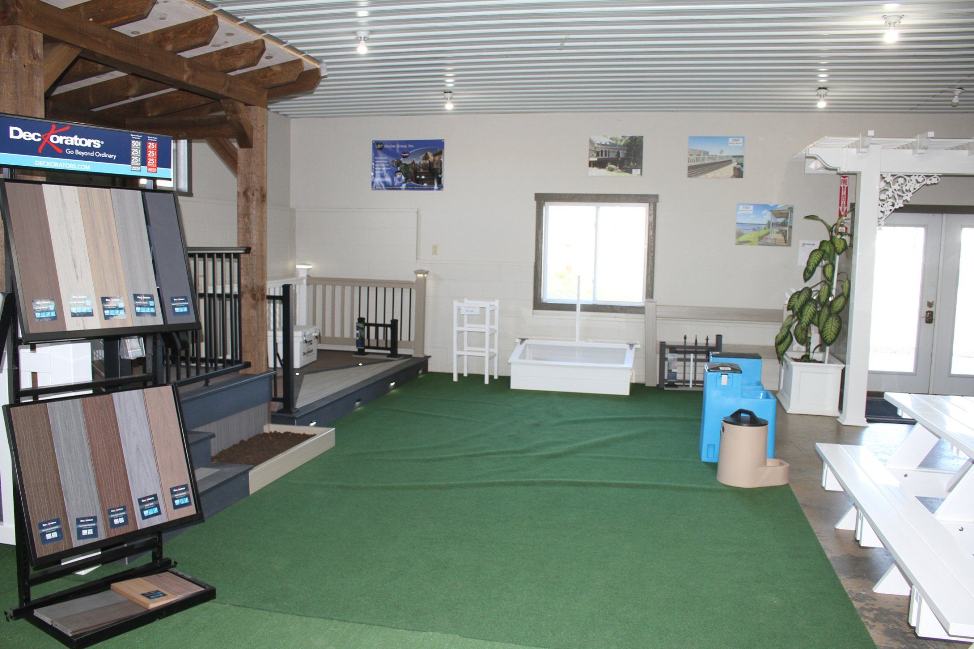 Interior of a showroom with deck and flooring samples, green carpet, and white furniture.