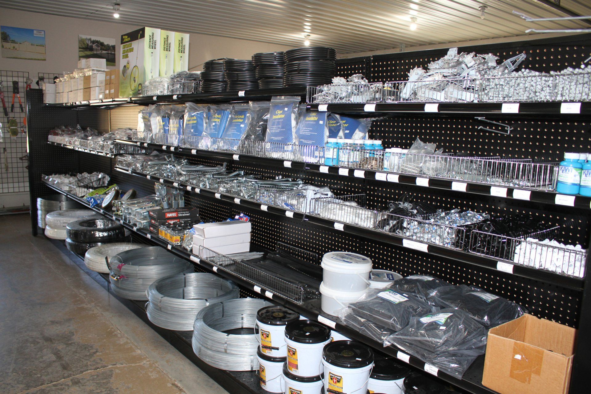 Shelves stocked with hardware and supplies in a store. Metal wire, hoses, and paint cans are visible.