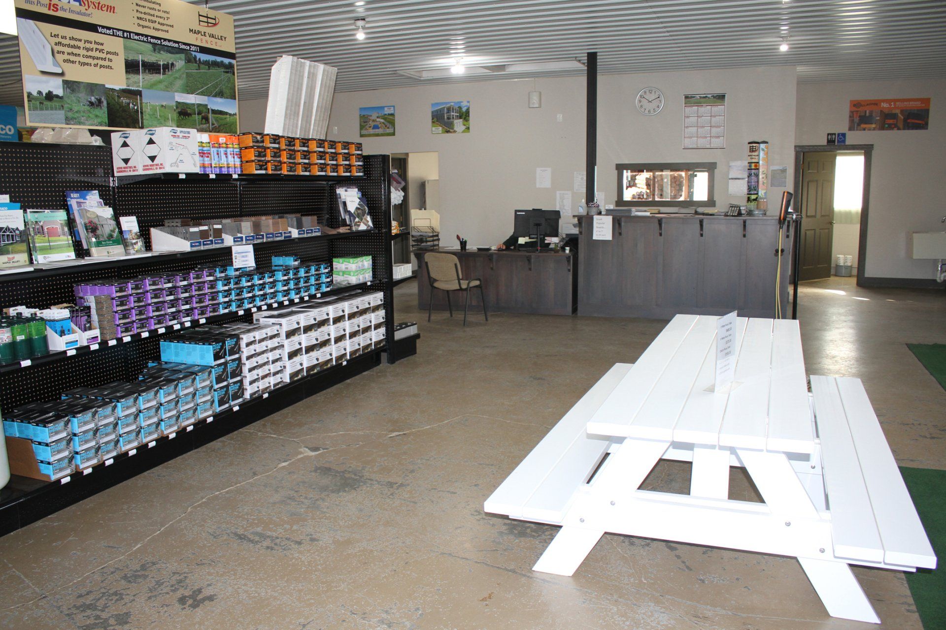 Interior of a store, featuring shelves of merchandise, a white picnic table, and a reception desk.