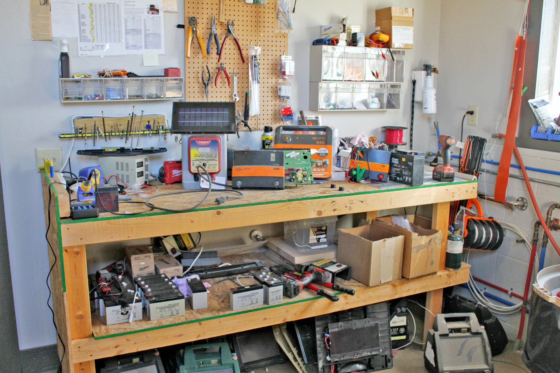 Workbench cluttered with electronics, tools, and parts in a garage.