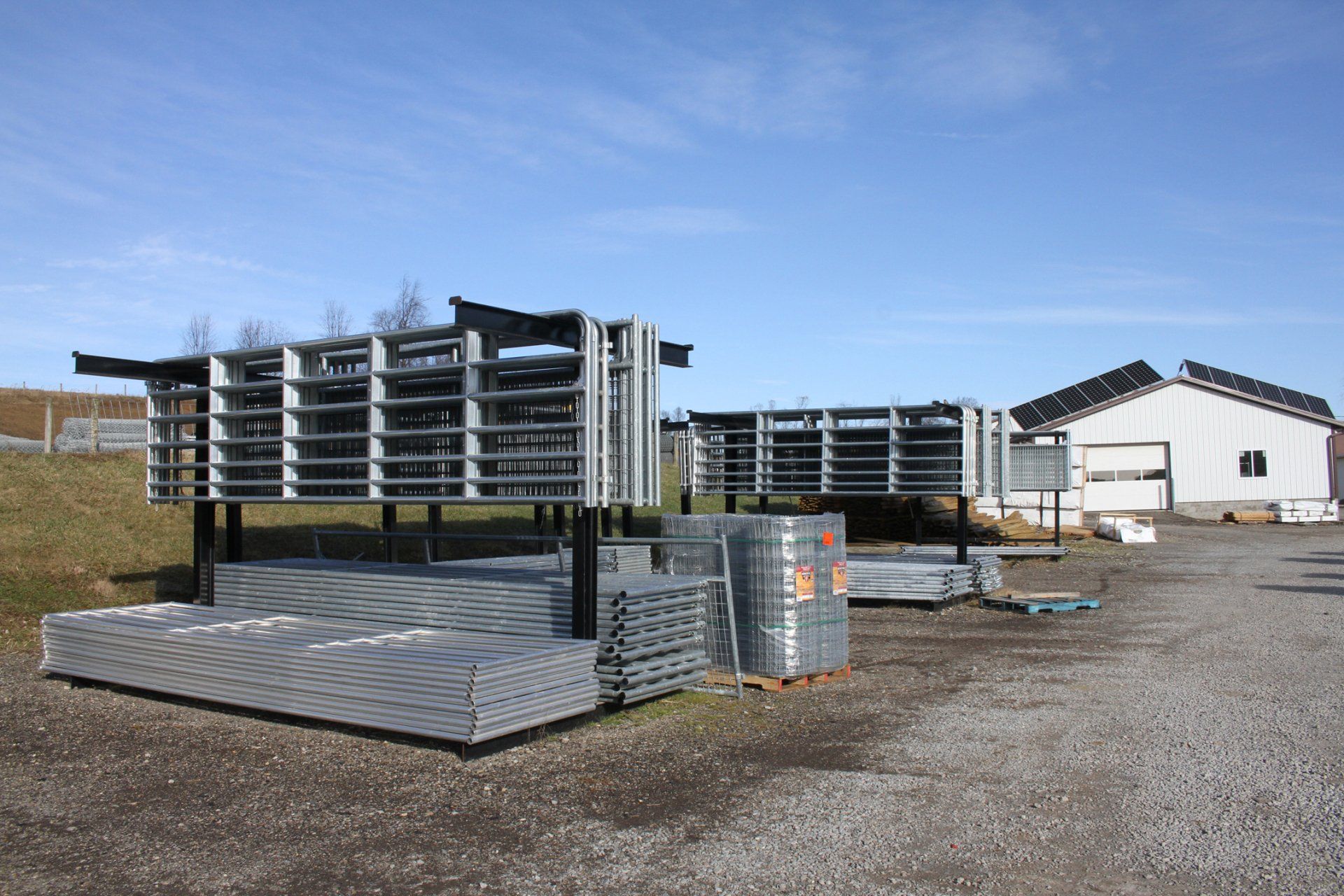 Stacks of metal fence panels and rolls of fencing materials in an outdoor storage area, with a building in the background.