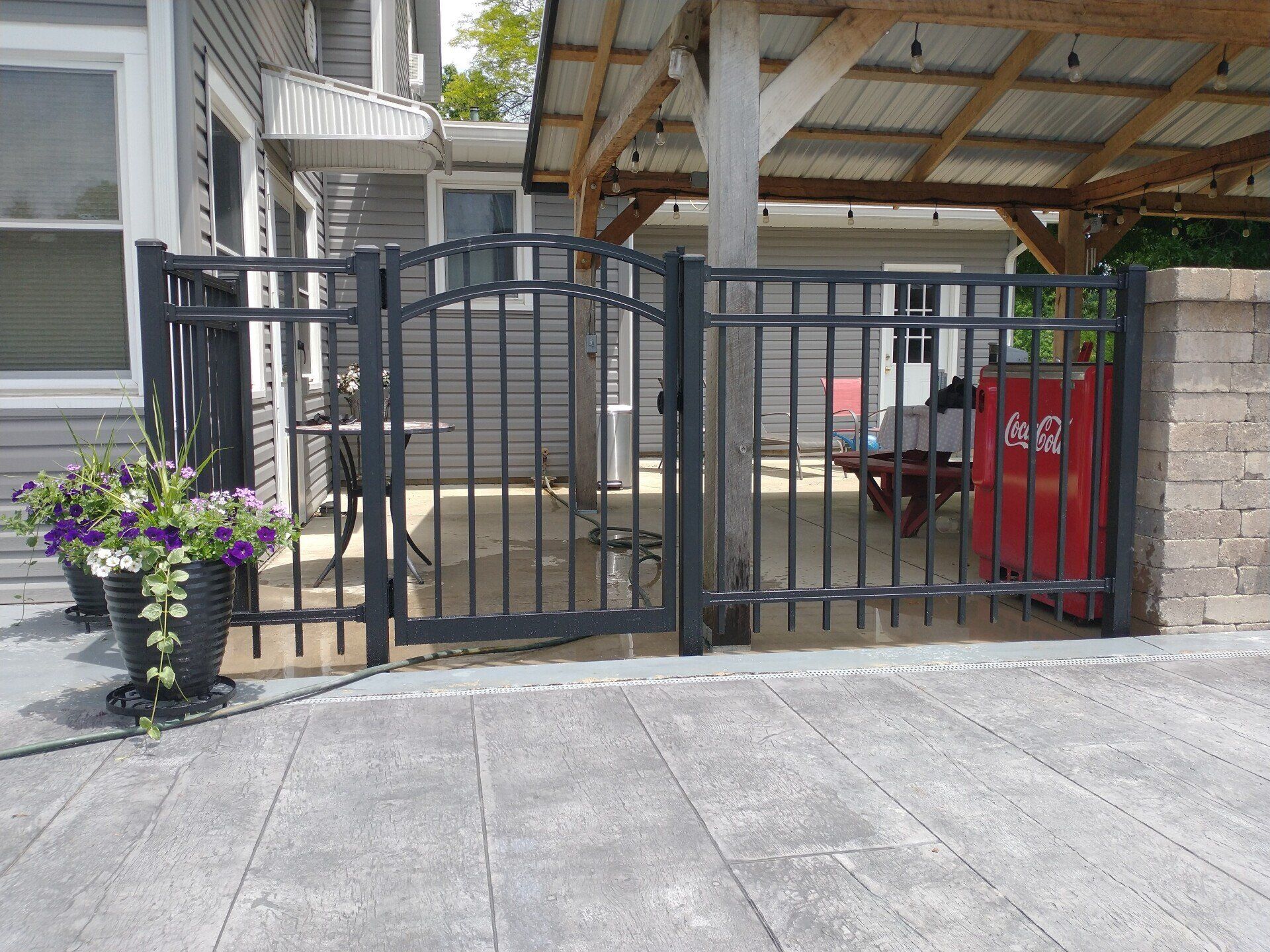 Black metal gate and fence enclose a patio area with tables and a red beverage cooler.