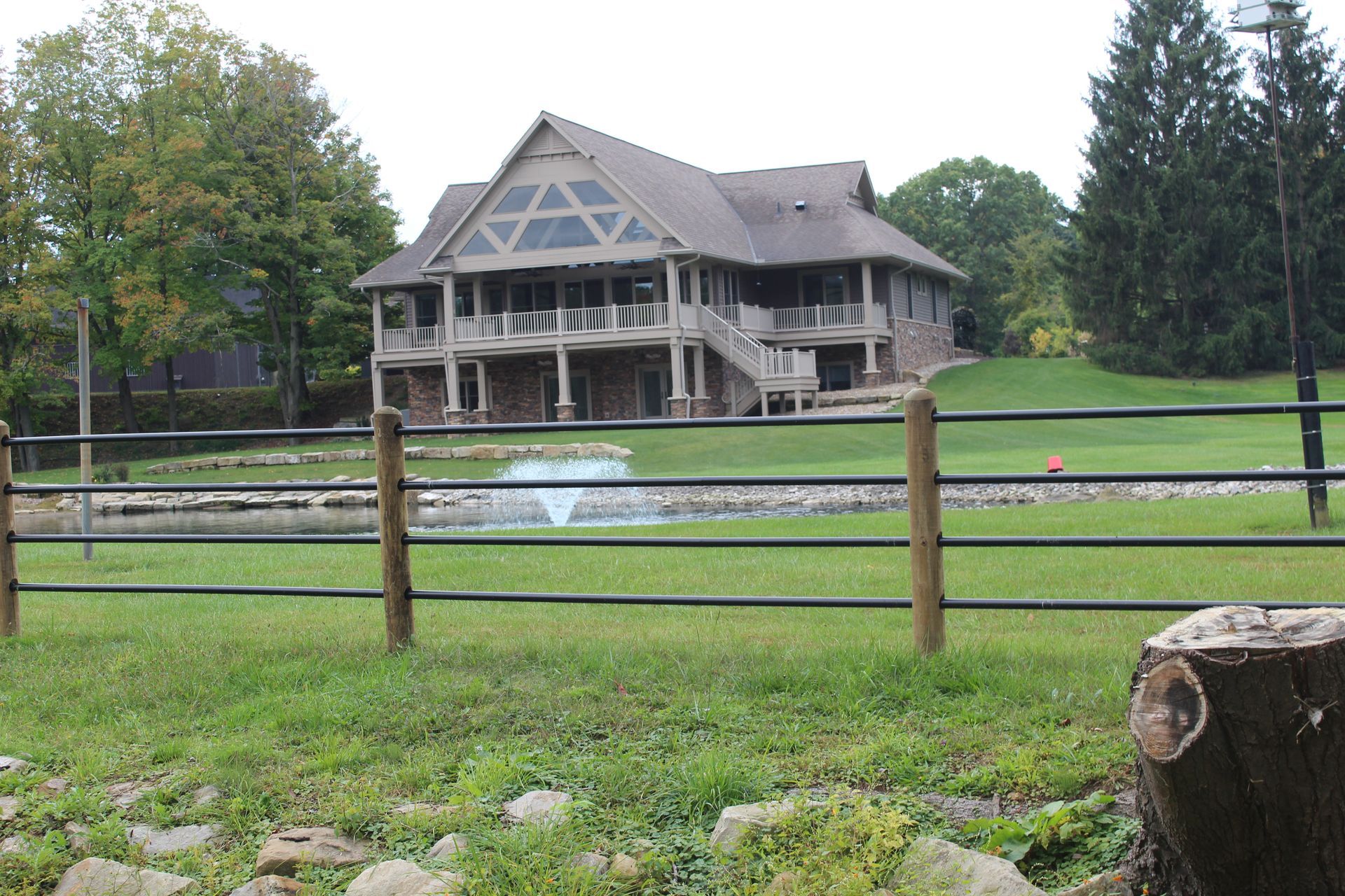 Large two-story house with a balcony and fountain in front of a fence and green grass.