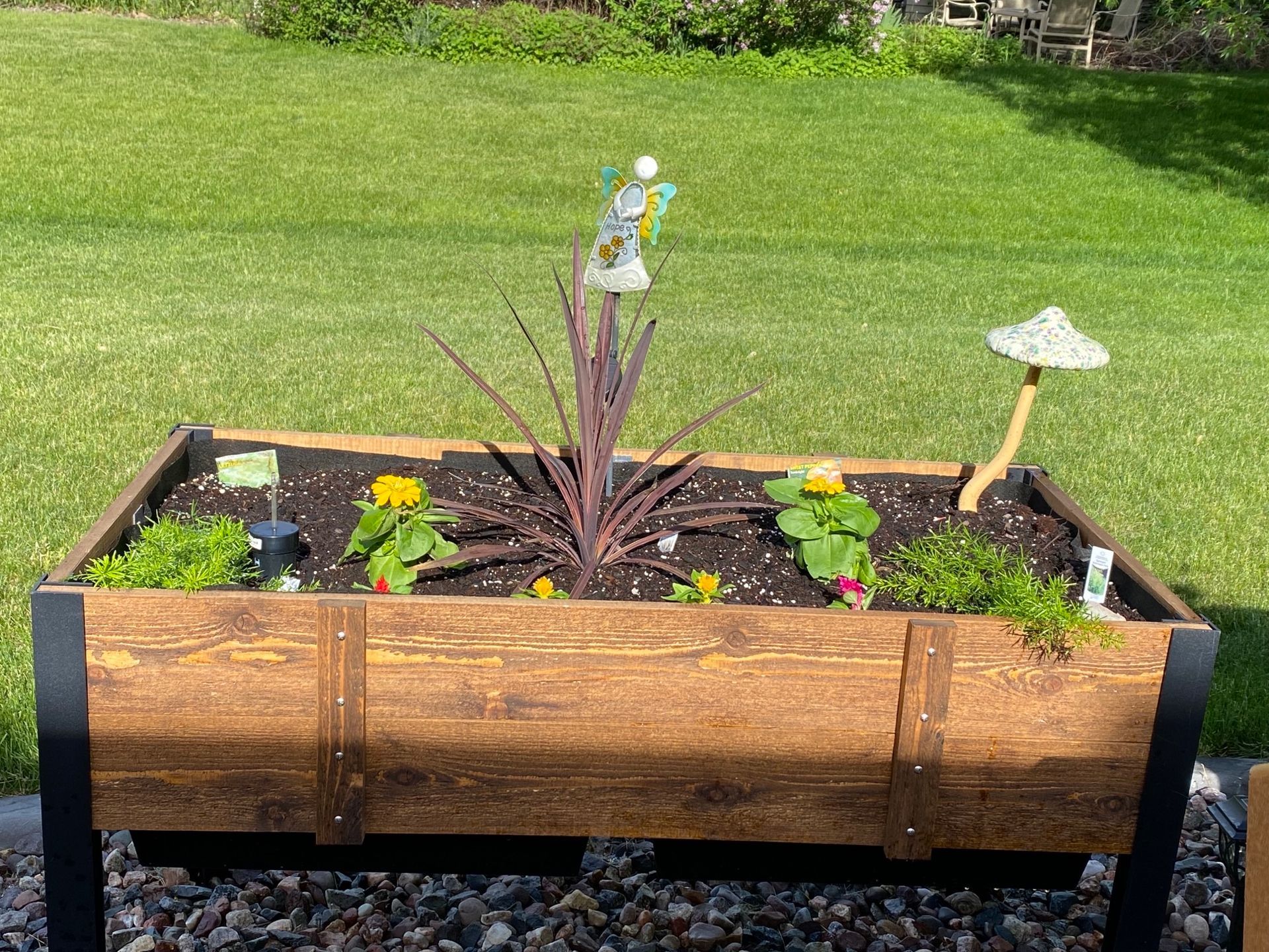 Wooden planter box with various plants and decorative mushroom on a green lawn.