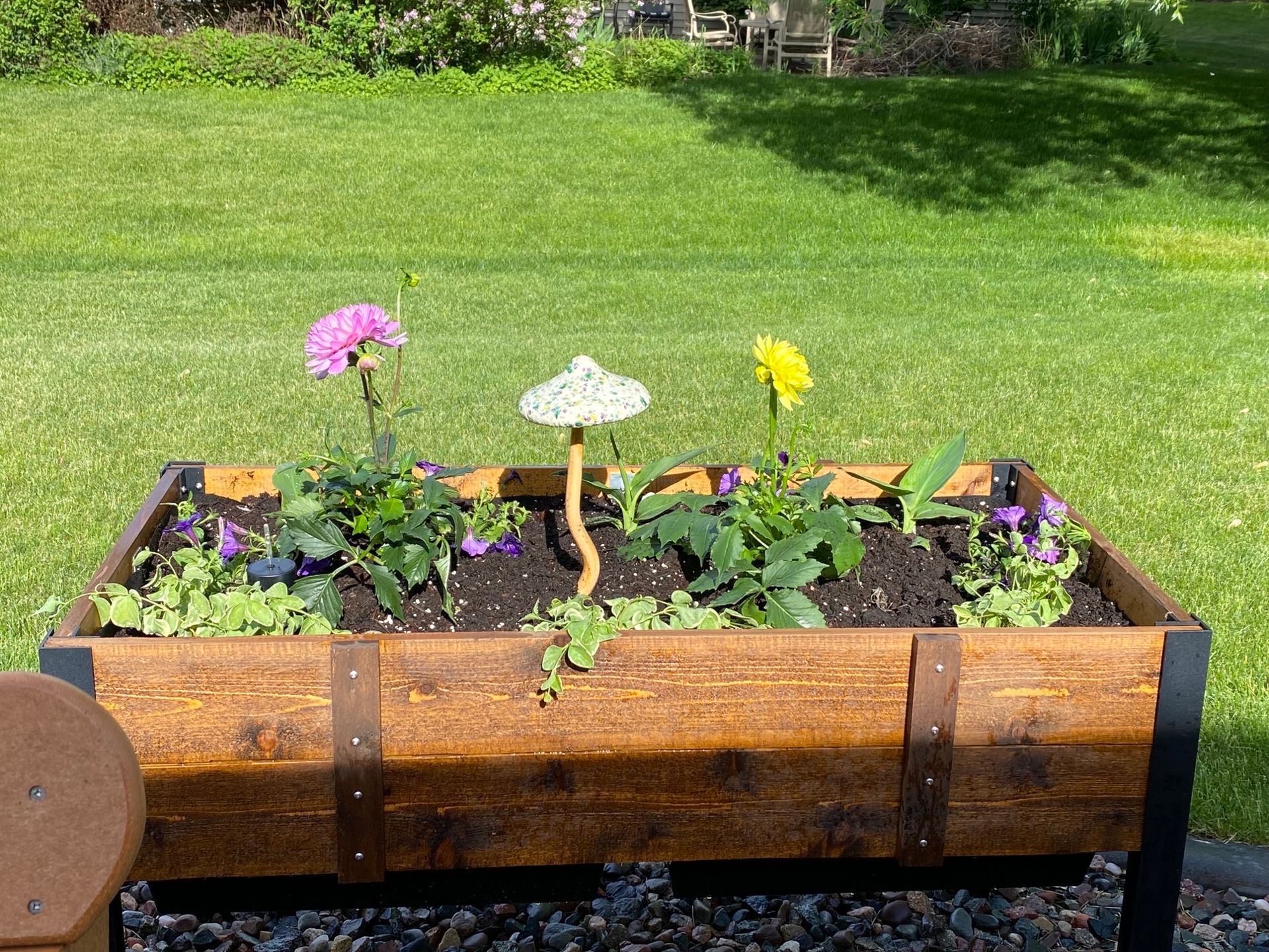 Wooden planter box with flowers and decorative mushroom on a grassy background.