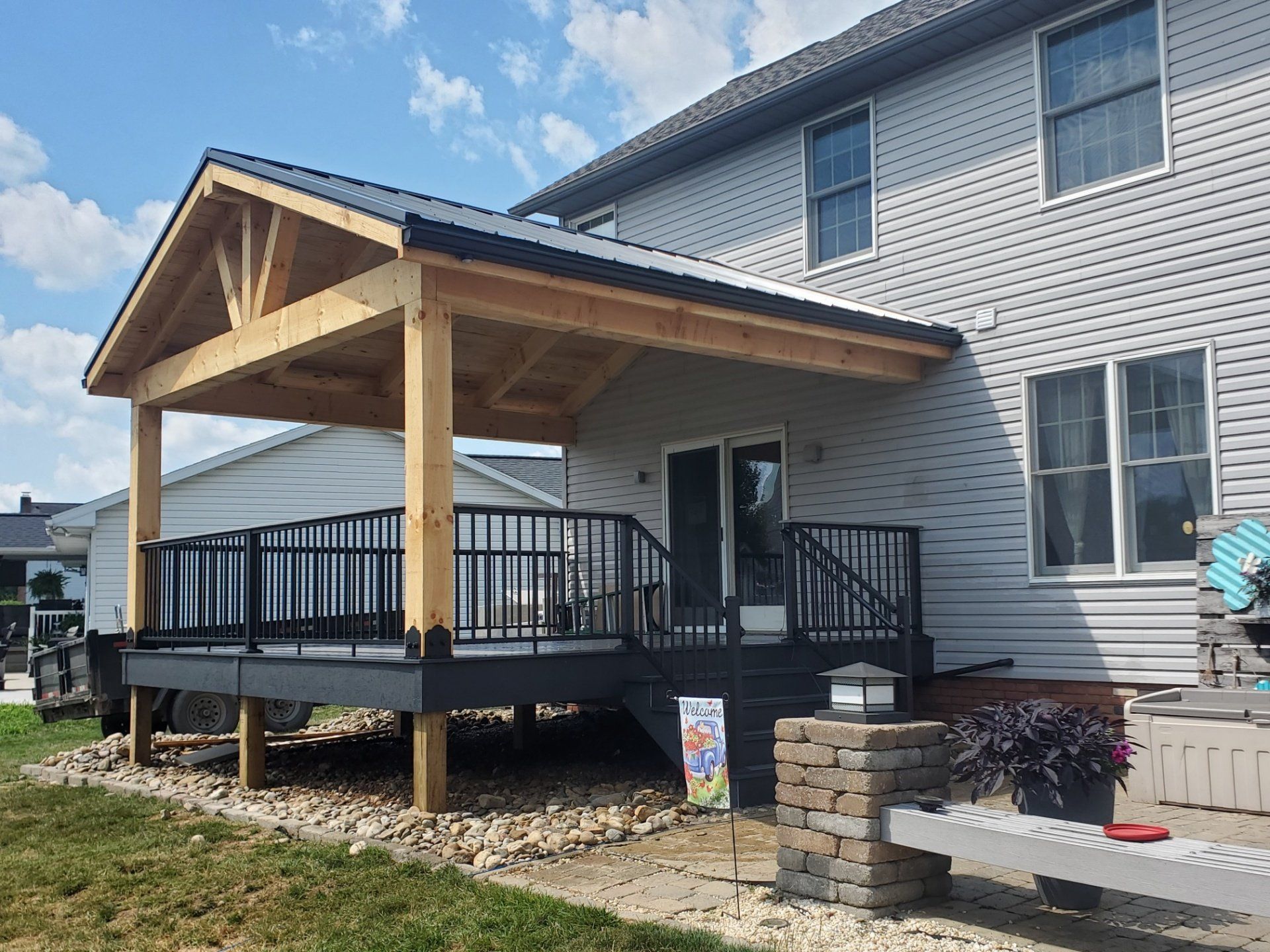 Wooden deck and covered patio extension on a two-story house with black railing and light gray siding.