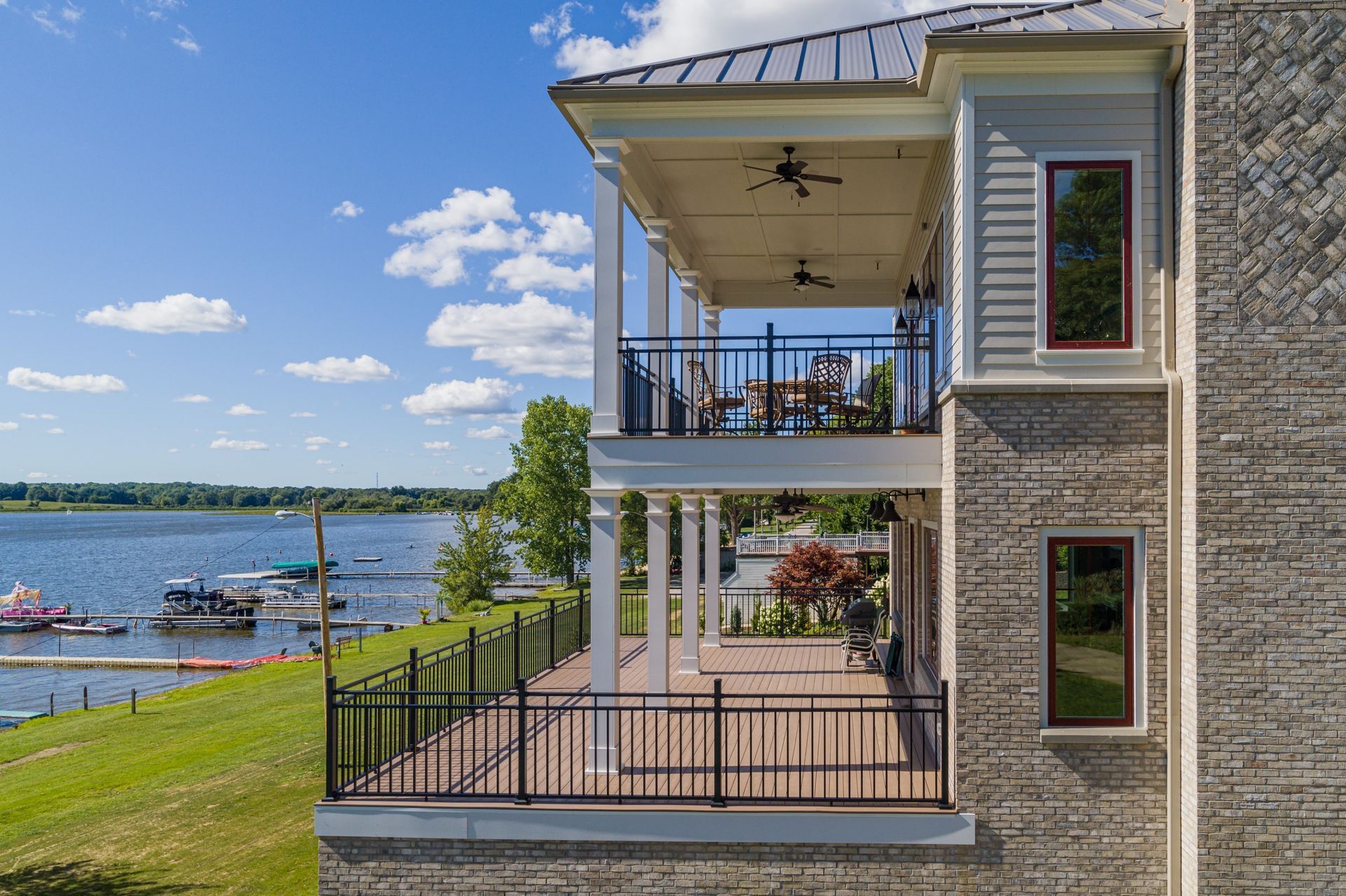 Two-story house with decks overlooking a lake, blue sky, and boats.