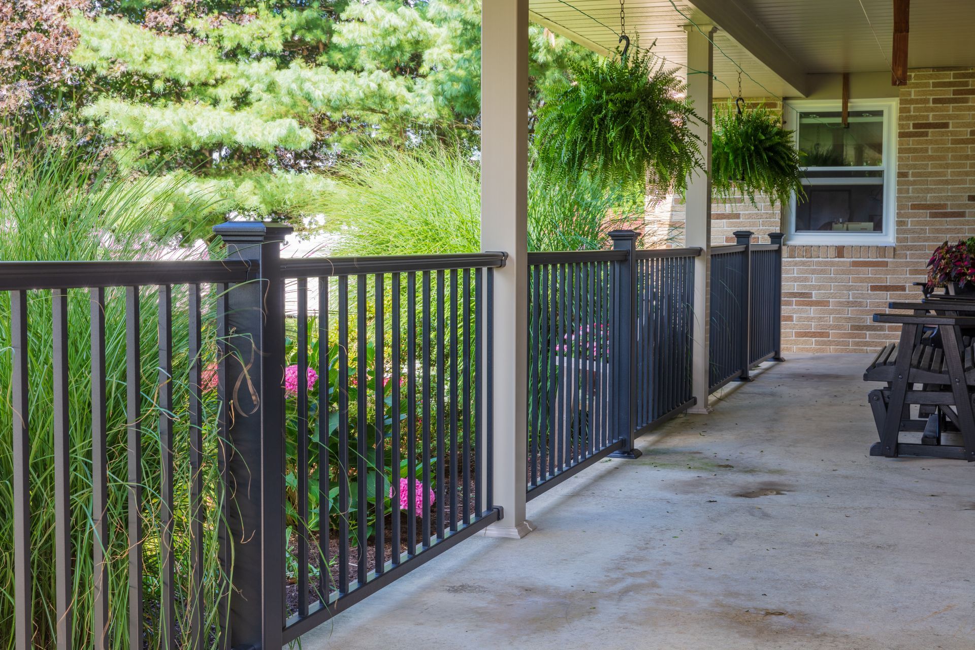 Black railing on a porch with hanging plants and lush greenery in the background.