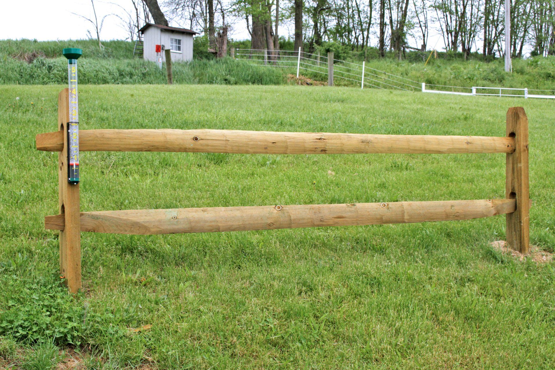 Wooden horse jump in a grassy field. A small building is visible in the background.