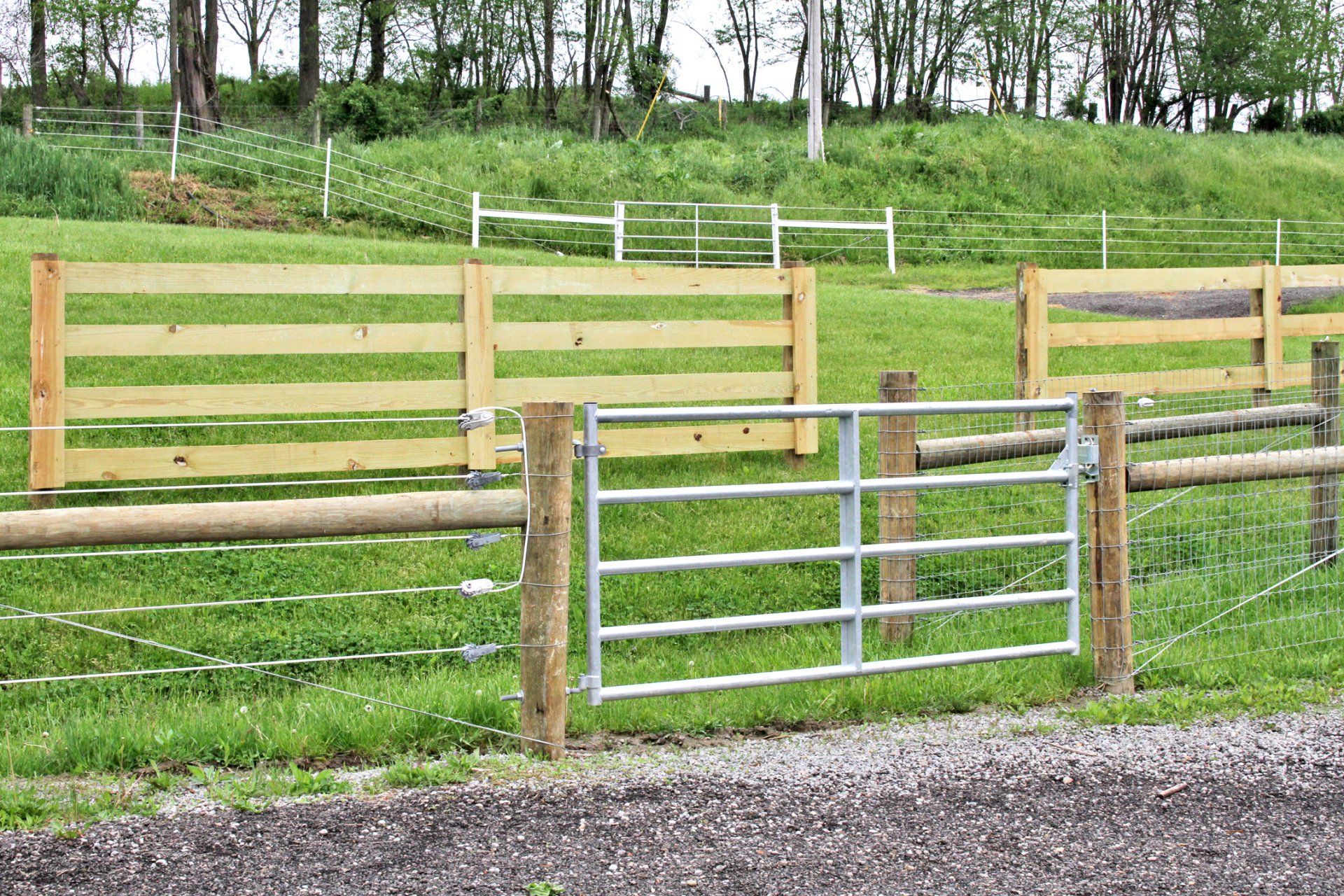 Wooden and wire fences with a metal gate in a grassy field.