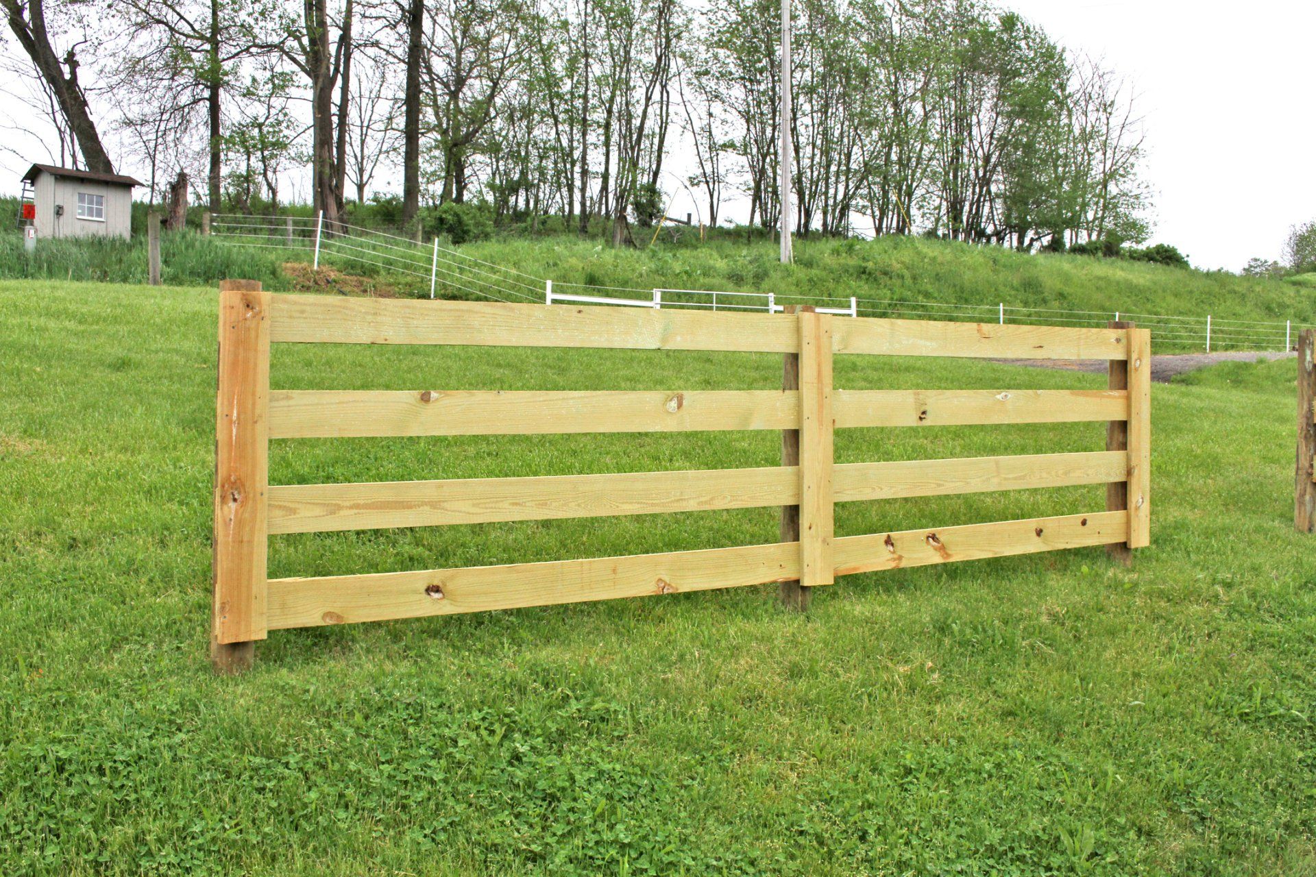 Wooden fence in grassy field with trees in the background.