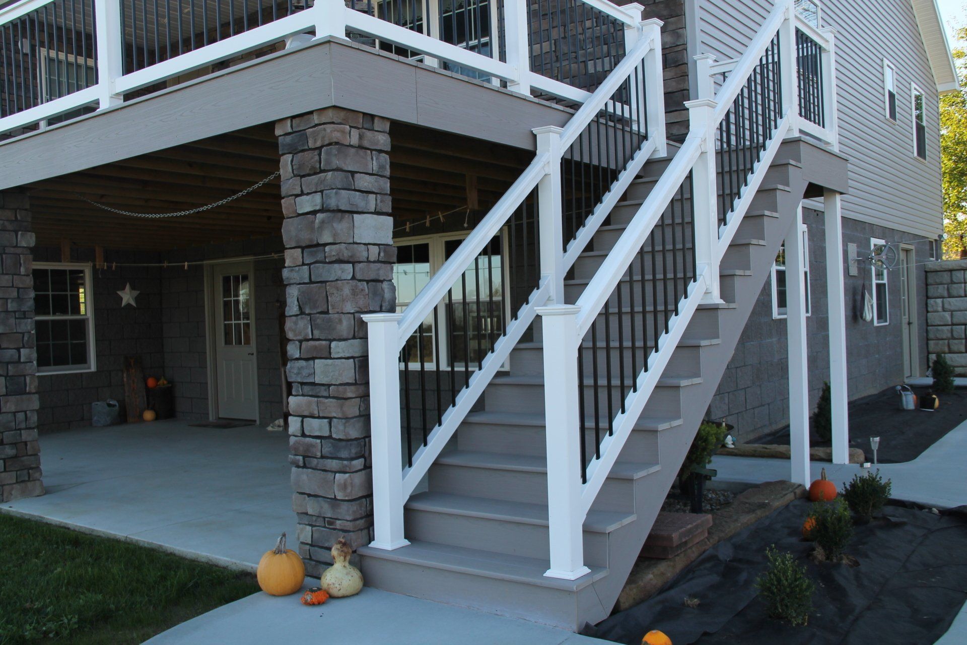 Exterior staircase with white railings, gray steps, and stone-covered support pillars leading to a deck.