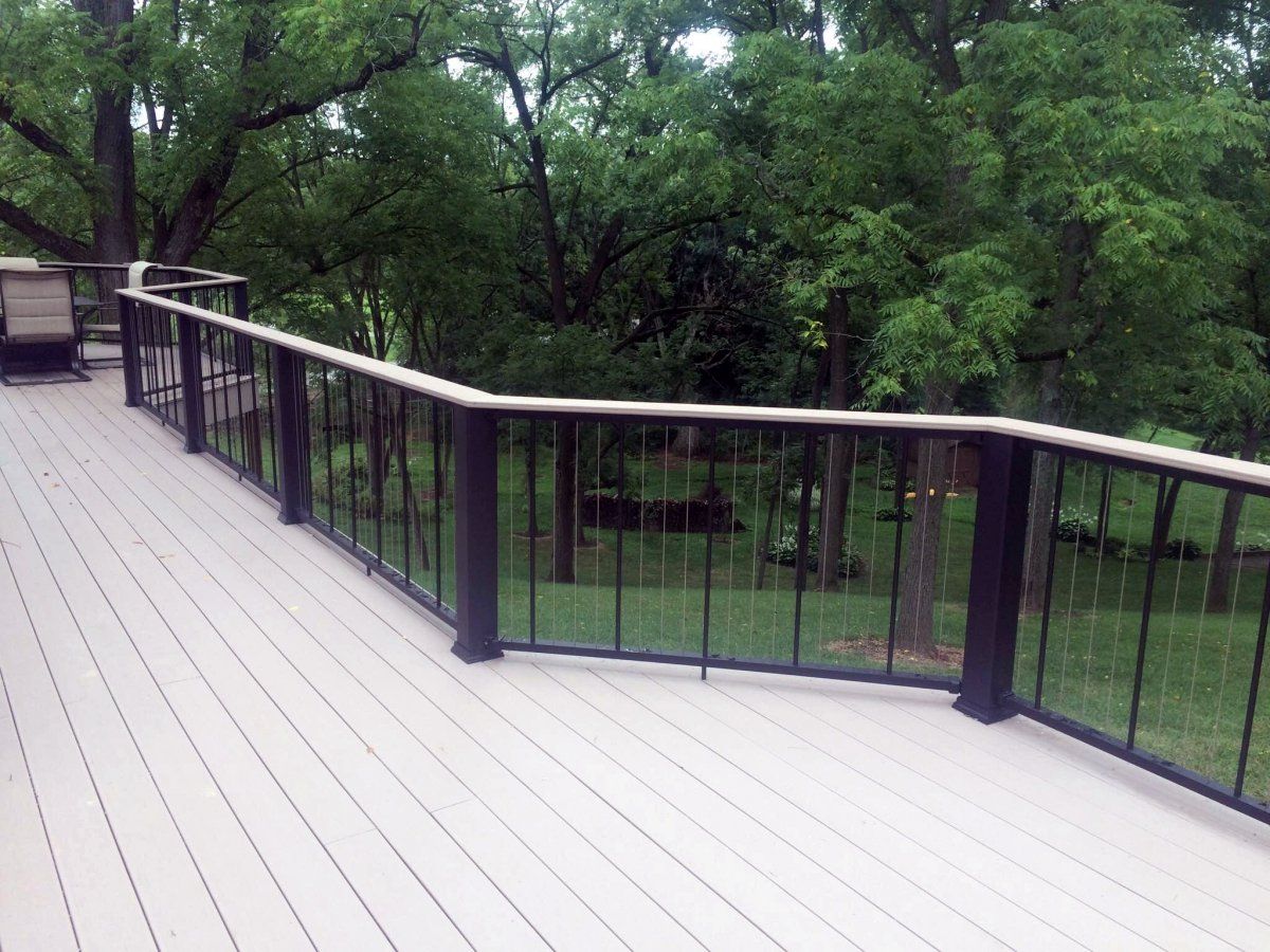 Wooden deck with black railings overlooking a green, wooded area.