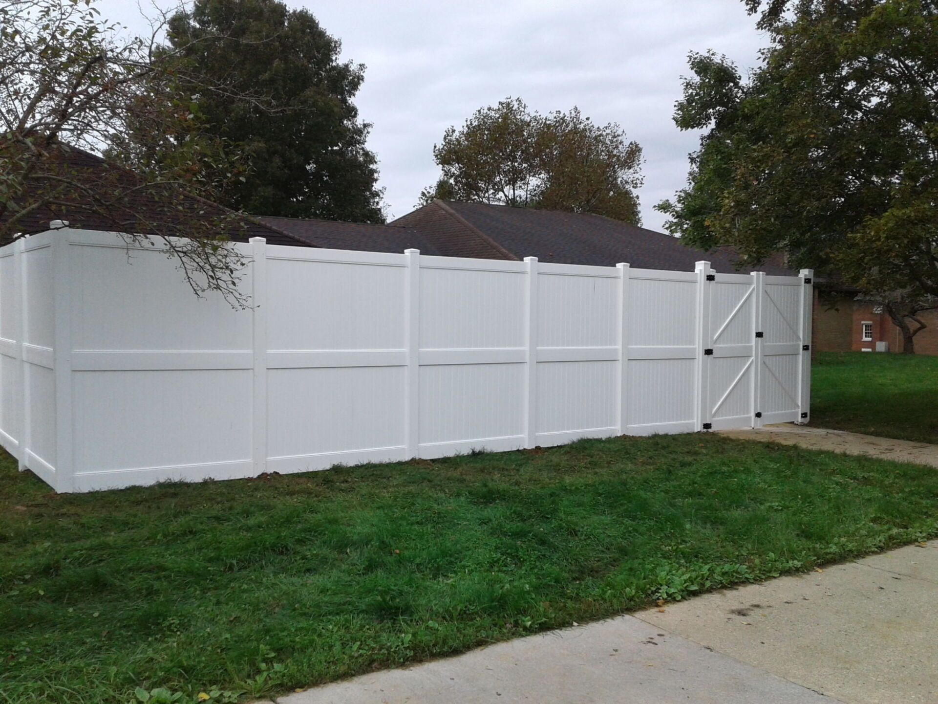 White vinyl privacy fence with gate in residential yard, overcast sky.