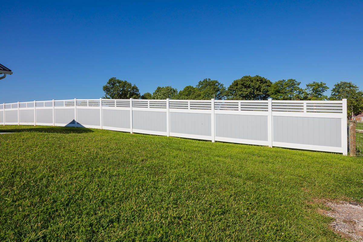 White vinyl fence on a grassy lawn under a clear blue sky.