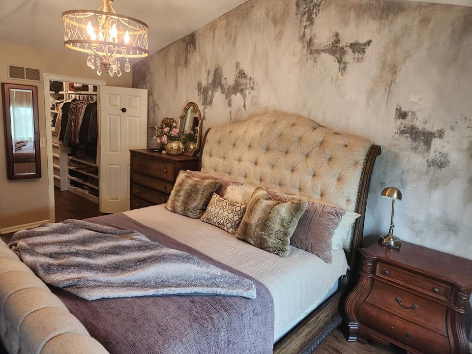 A bedroom with a bed , nightstand , mirror and chandelier.