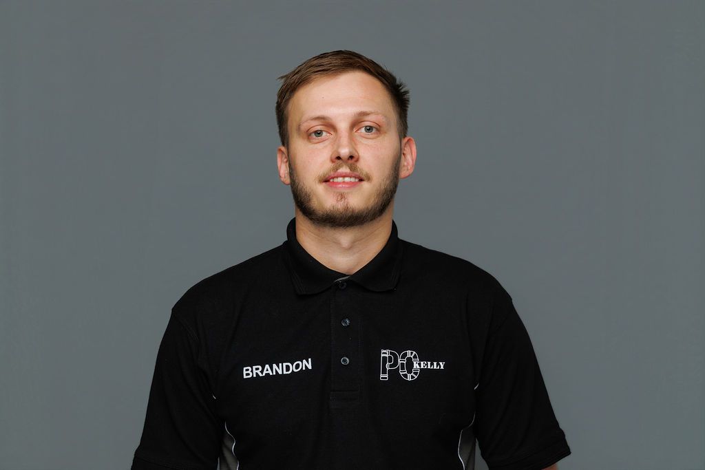 Man in a black collared shirt standing against a gray background