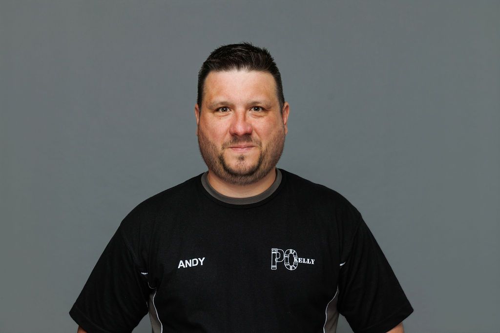 Man standing against a gray background wearing a black shirt with a neutral expression