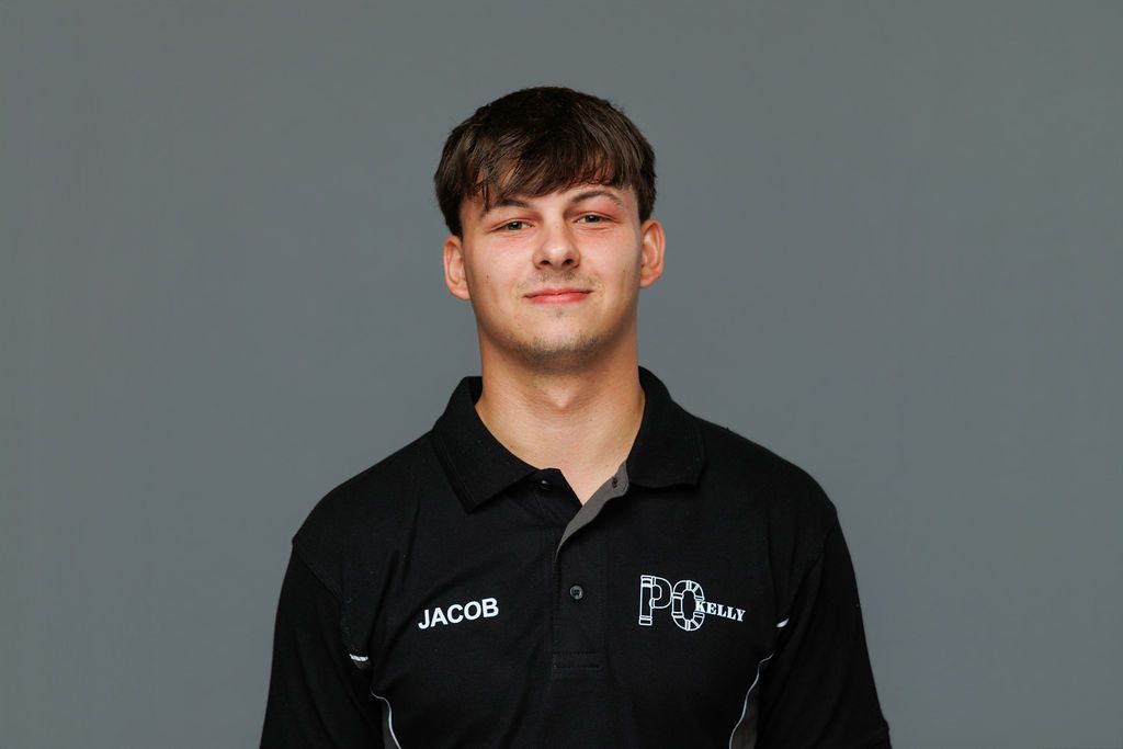 Man in a black polo shirt standing against a plain gray background.