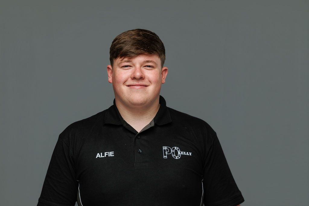 Person in a black polo shirt against a gray background, smiling at the camera.