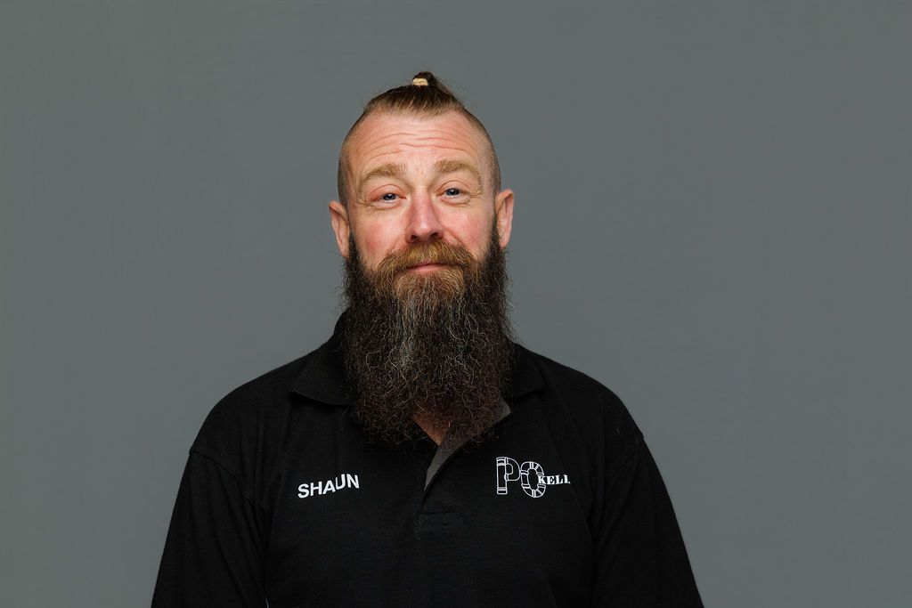 Man with a long beard wearing a black collared shirt against a gray background