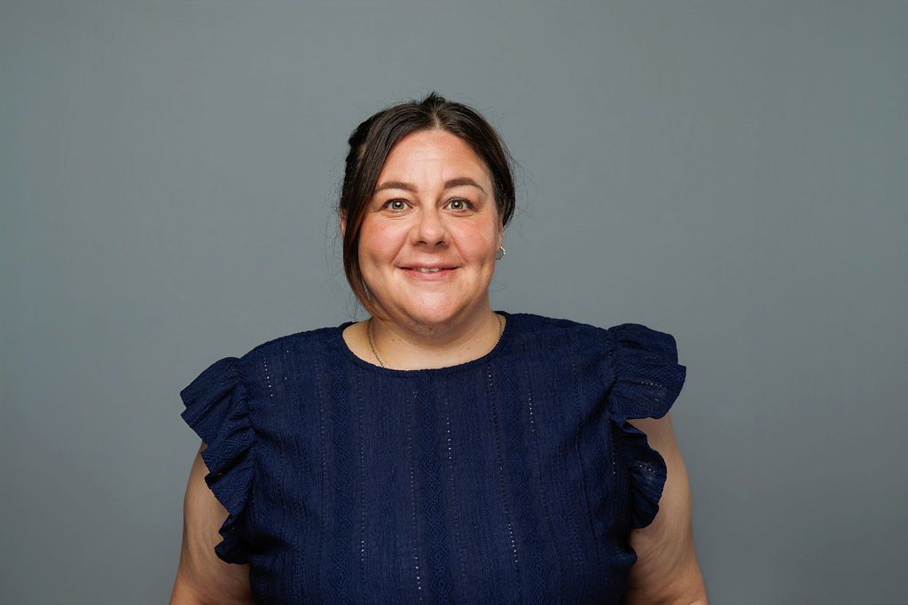 Smiling person in a navy blue ruffled top against a plain gray background