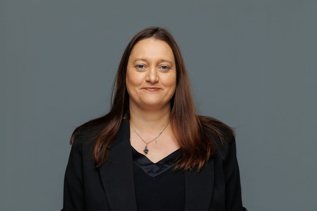 Portrait of a person in a black blazer against a gray background