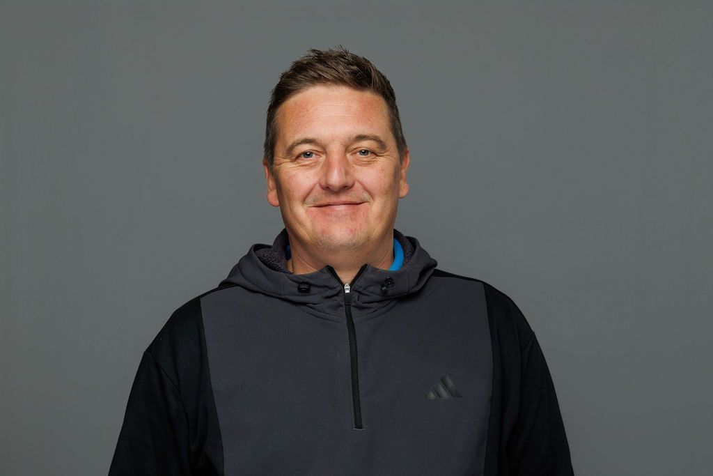 Man in a dark jacket smiling against a plain gray background