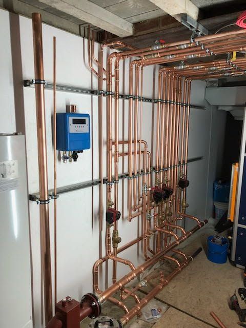Copper plumbing pipes and valves in a utility room with a blue control box on the wall.