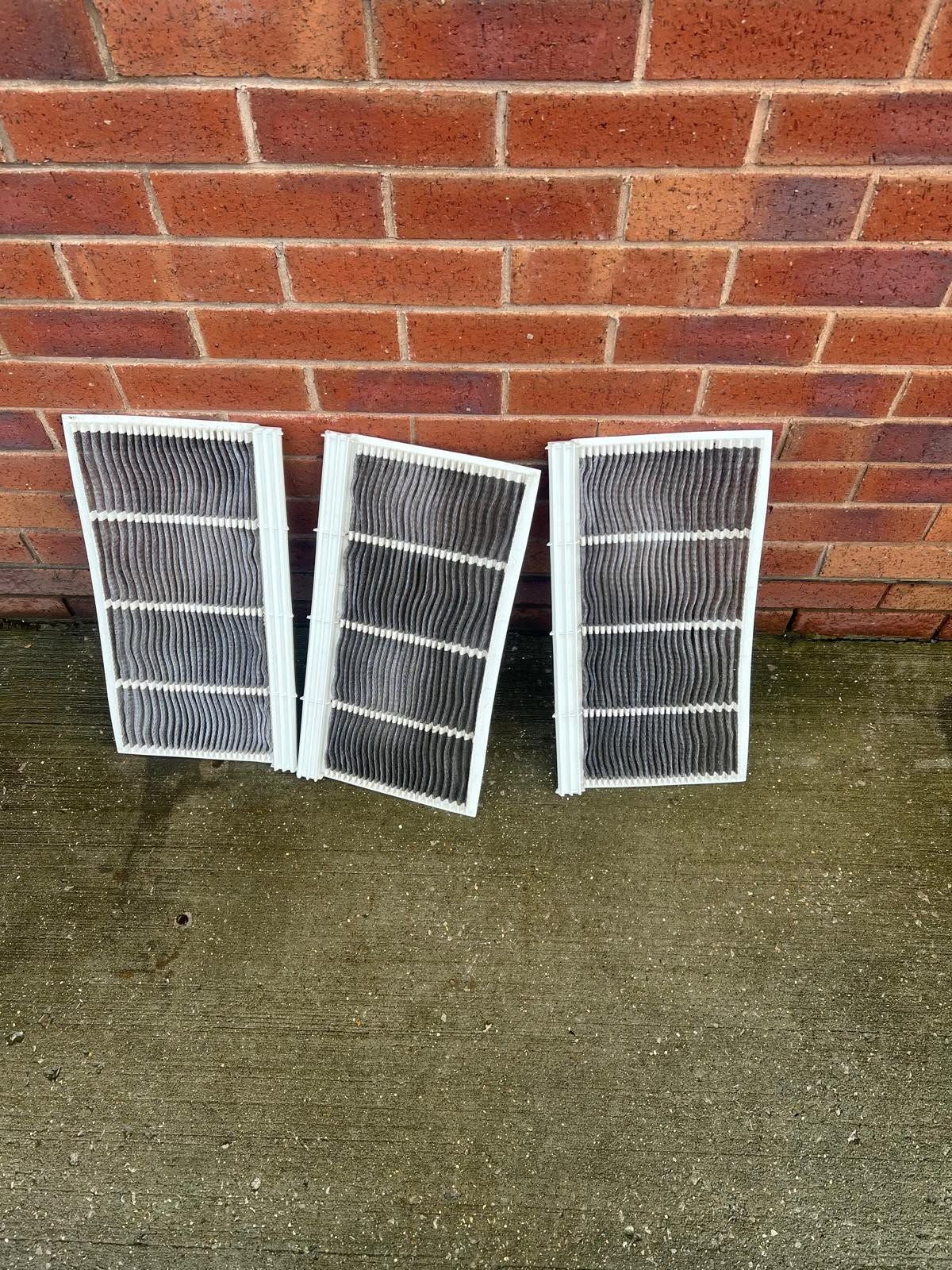 Three white air filters leaning against a red brick wall on wet concrete.
