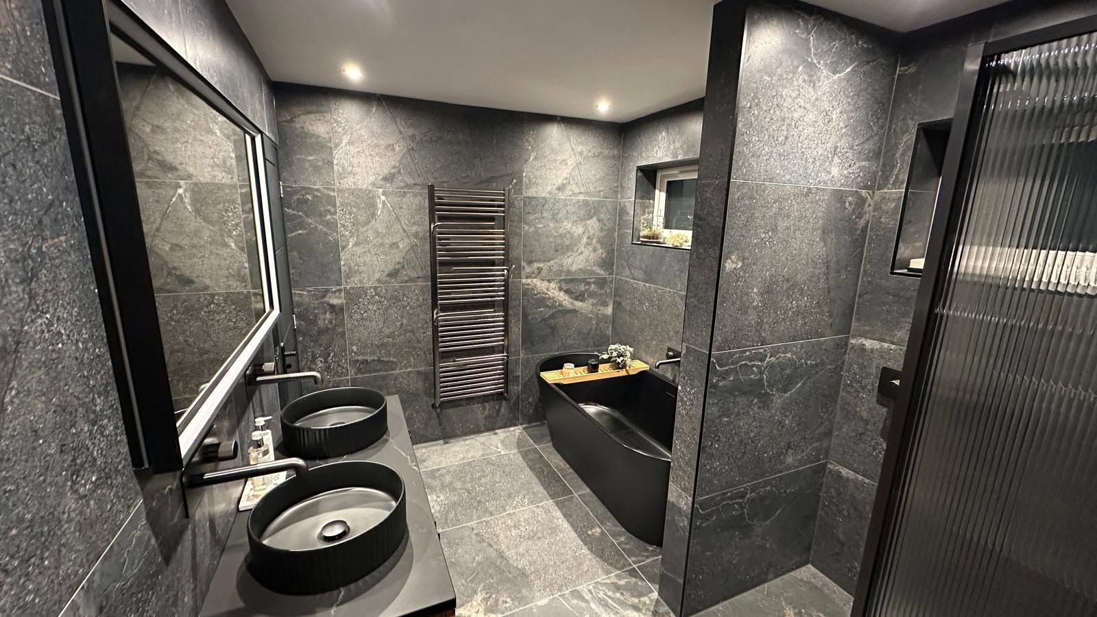 Modern black-and-gray bathroom with double sinks, shower, and walk-in vanity area