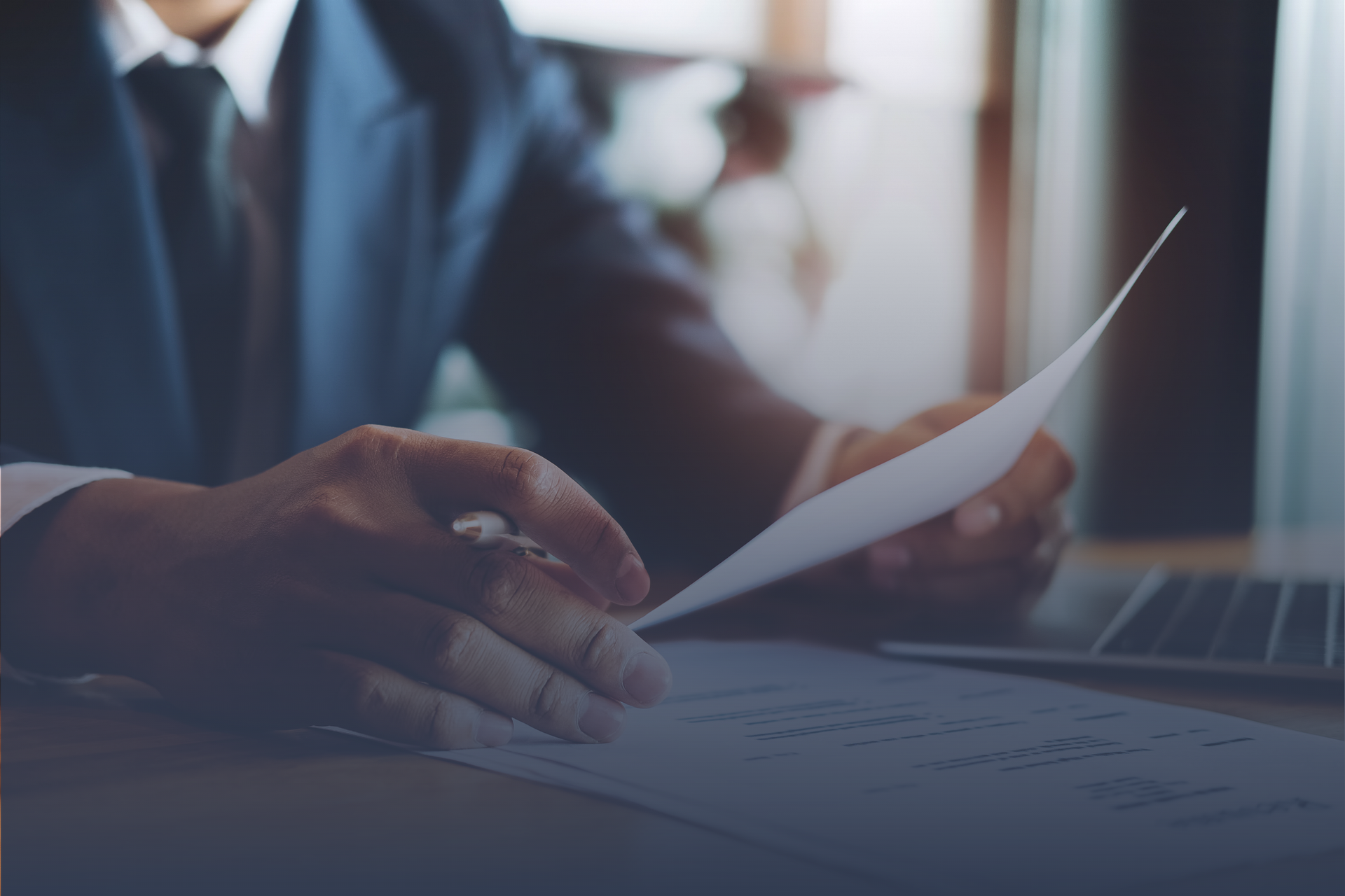 Person in a suit holding a document, working at a desk with a laptop. NearTech Search logo.