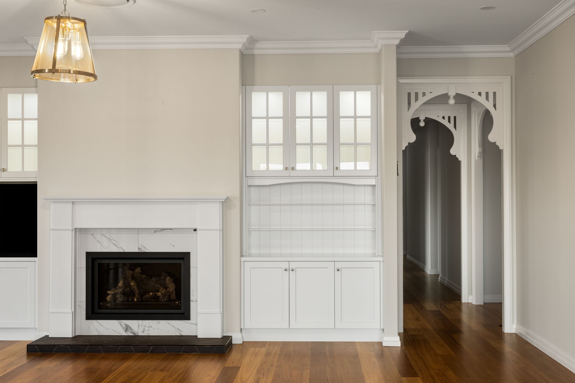 Living room with fireplace, built-in cabinets, and arched doorway, all painted white. Wooden floor.