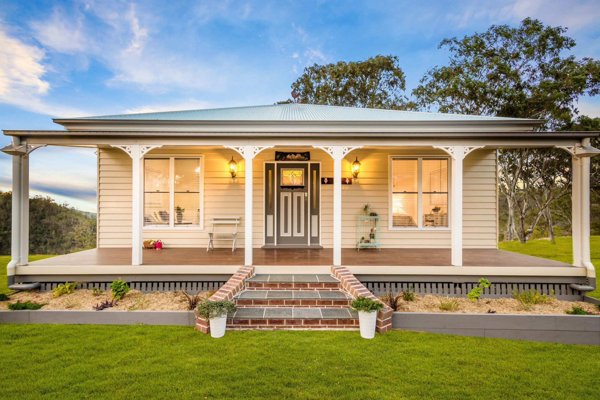 Cream-colored cottage with porch, steps, and front door, set in a grassy yard under a blue sky.