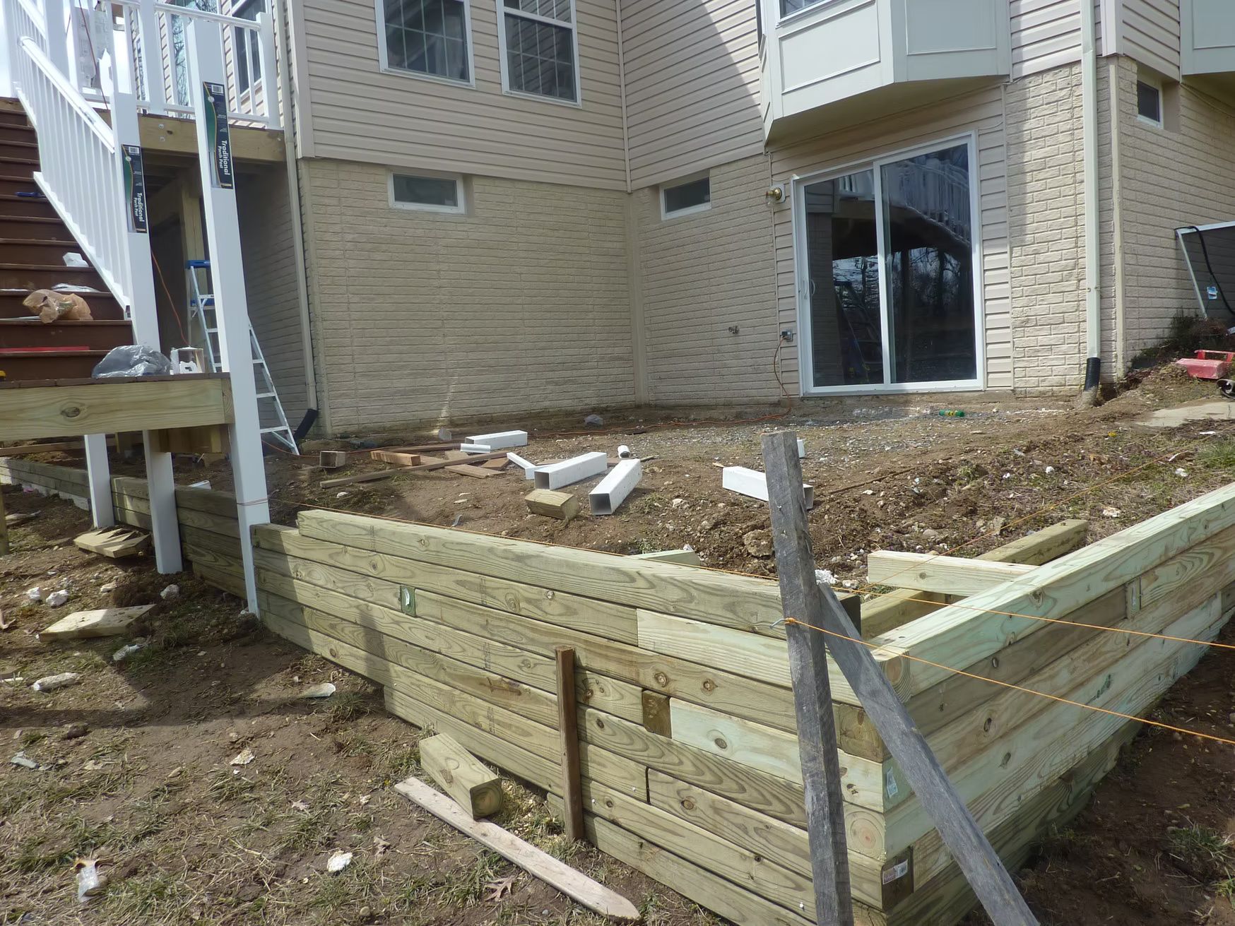 Raised wooden garden bed beside a brick house with a sliding glass door and bare soil inside